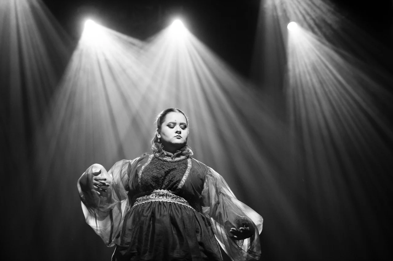 Eli Rivera performing beneath dramatic beams of stage lighting, photographed in black and white